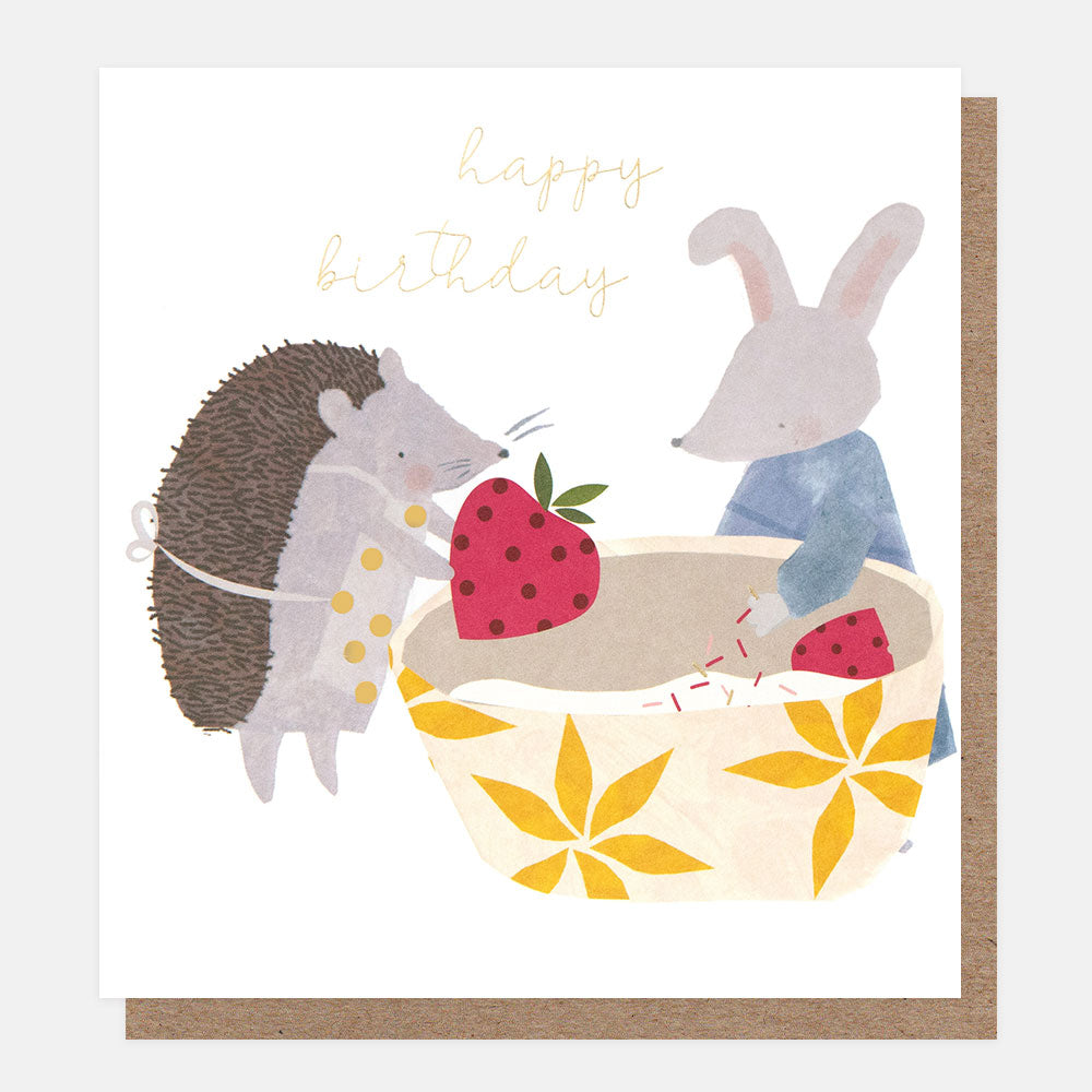 birthday card featuring a hedgehog and a rabbit putting strawberries into a baking bowl, and the words happy birthday in gold script