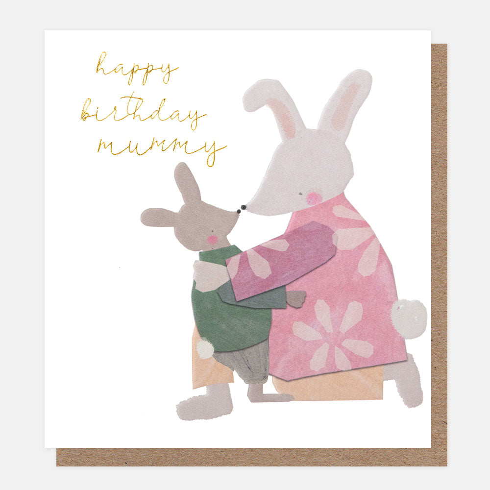A white greetings card with a mother rabbit in a pink floral dress cuddling a little rabbit and the text 'happy birthday mummy' in gold foil script, shown with a brown kraft envelope behind it.