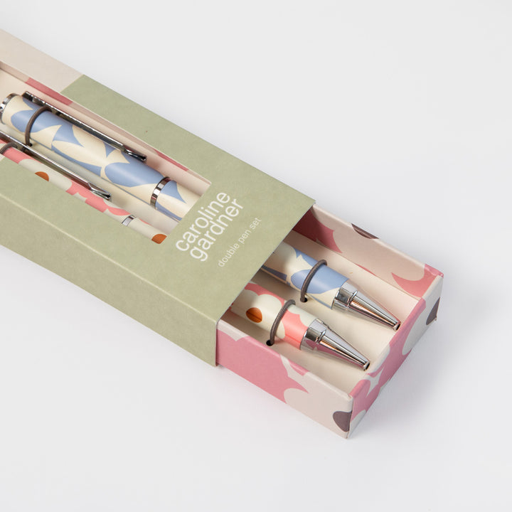 A boxed set of two decorative pens with a pastel camouflage pattern, shown partially inside a matching patterned box on a light gray background.