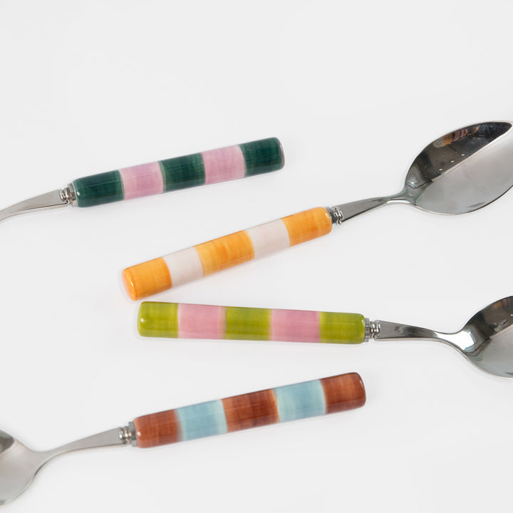 Four metal spoons with colorful striped handles arranged diagonally on a plain white background.