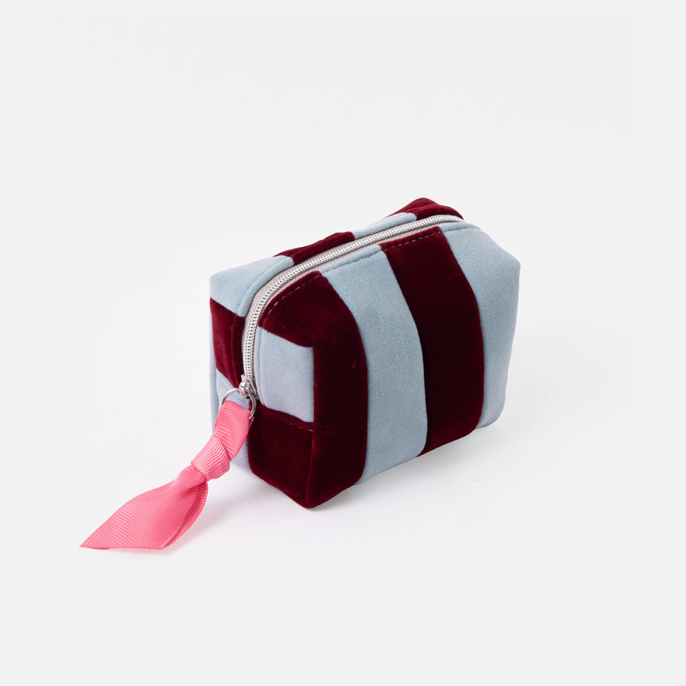 A small zippered cosmetic pouch with alternating vertical stripes of dusty light blue and deep burgundy velvet, featuring a bright pink ribbon pull on a white background.