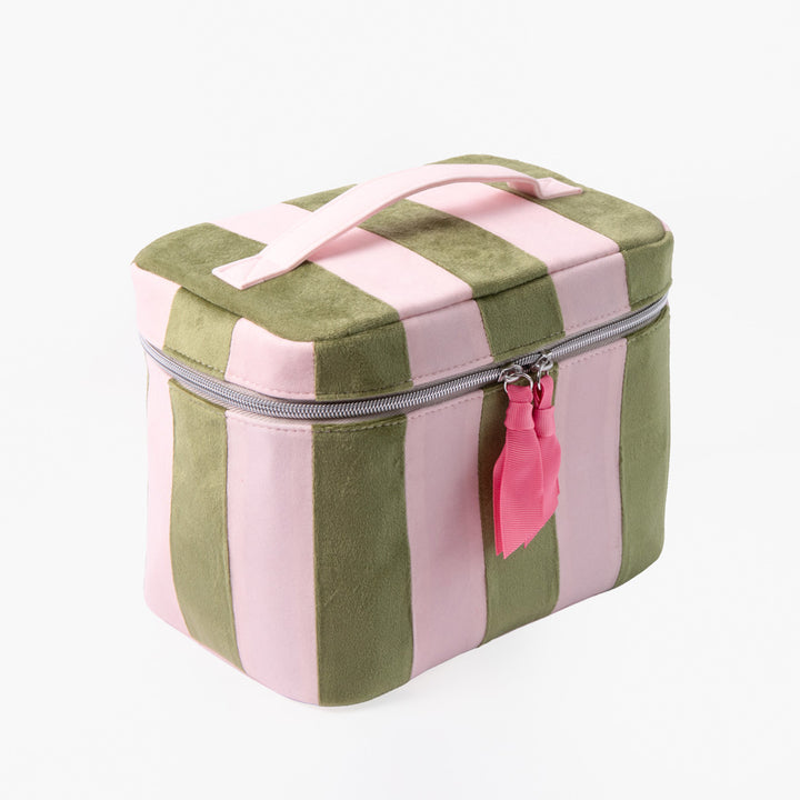 A square zippered vanity case with vertical pink and olive green stripes, featuring a light pink top handle and a pink tassel charm on the zipper.
