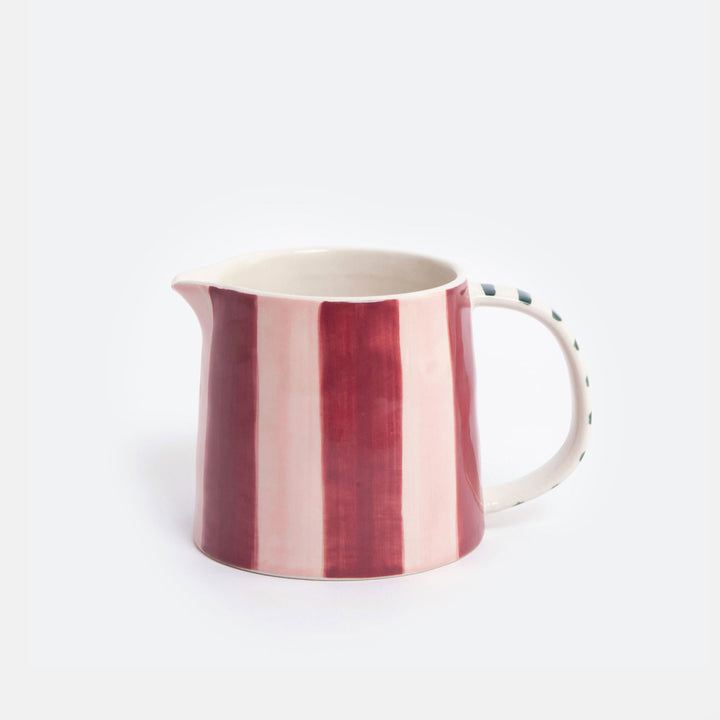 A ceramic jug with vertical stripes in deep red and light pink on the exterior, with a white handle and a dotted pattern on the side, set against a plain light gray background.