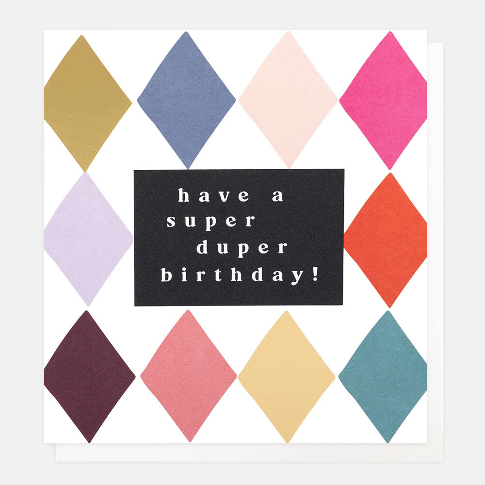 A greetings card with a colourful harlequin diamond pattern including gold foil and the text 'have a super duper birthday!' in white lettering on a black panel, shown with a white envelope behind it.