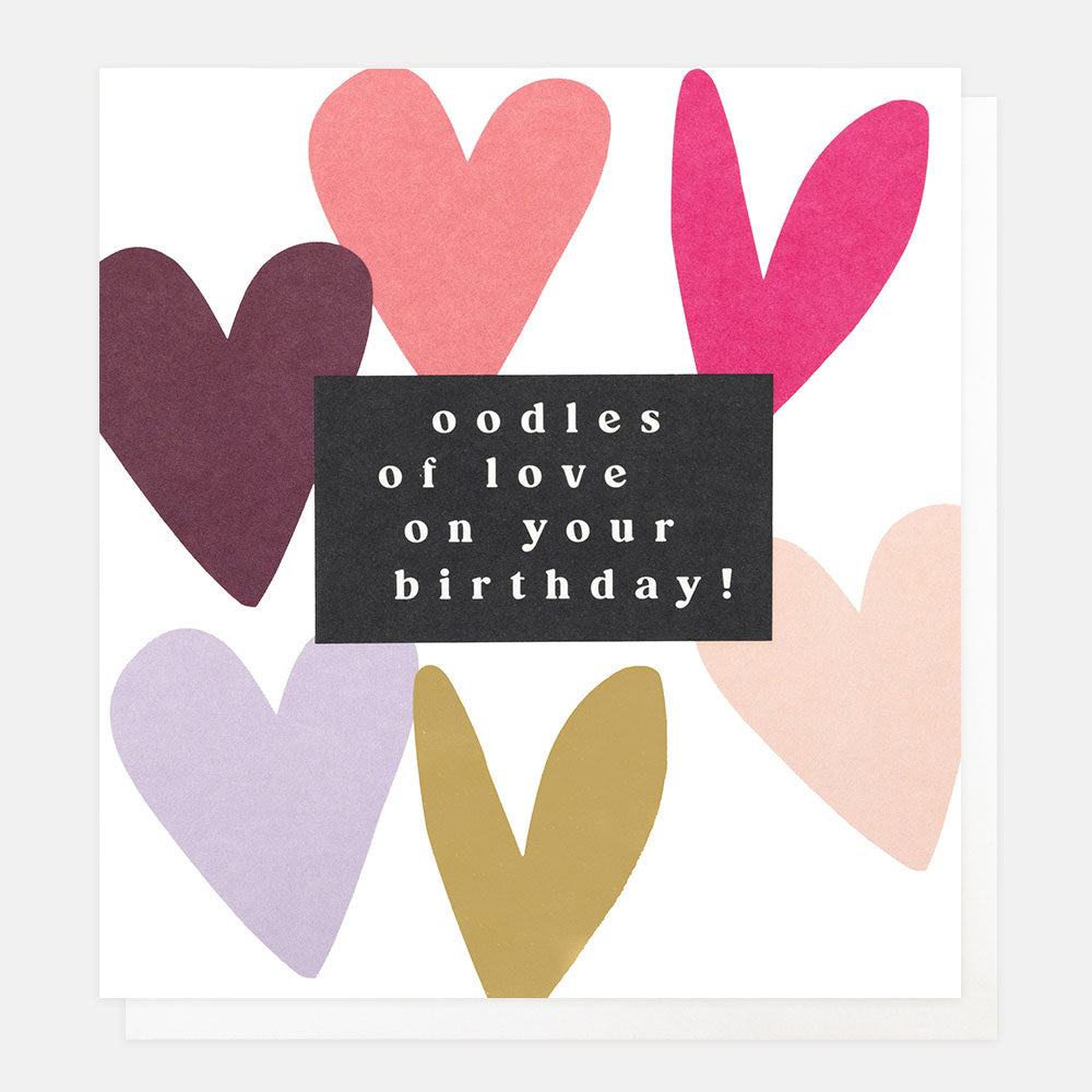 A white greetings card with colourful and gold foil hearts and the text 'oodles of love on your birthday!' in white lettering on a black panel, shown with a white envelope behind it.