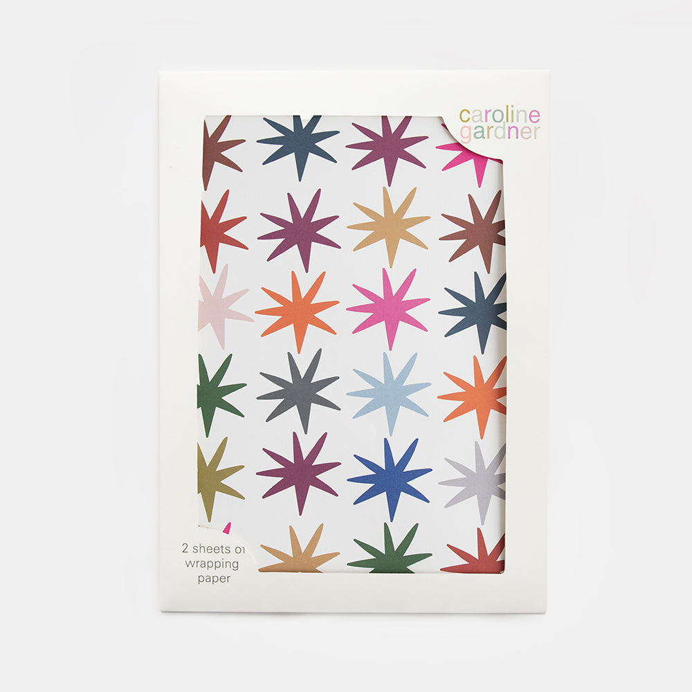 A pack of Caroline Garonier wrapping paper in a white sleeve, featuring a pattern of colorful eight-pointed stars in various shades including pink, blue, green, orange, and purple.