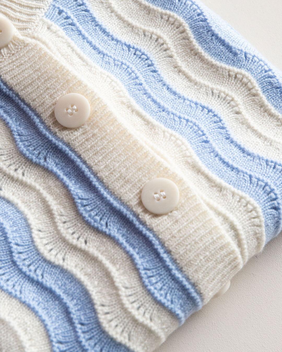 Close-up of a knitted cardigan with blue and white wave stripes and buttons.