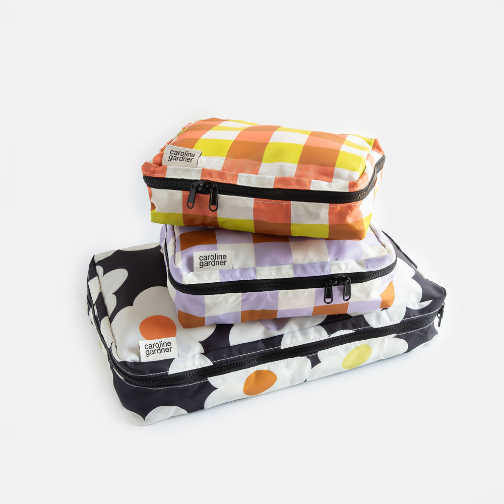 set of 3 packing cubes. 1 large in a cream flowers on a charcoal background design and 2 smaller cubes in lilac and yellow/orange check designs