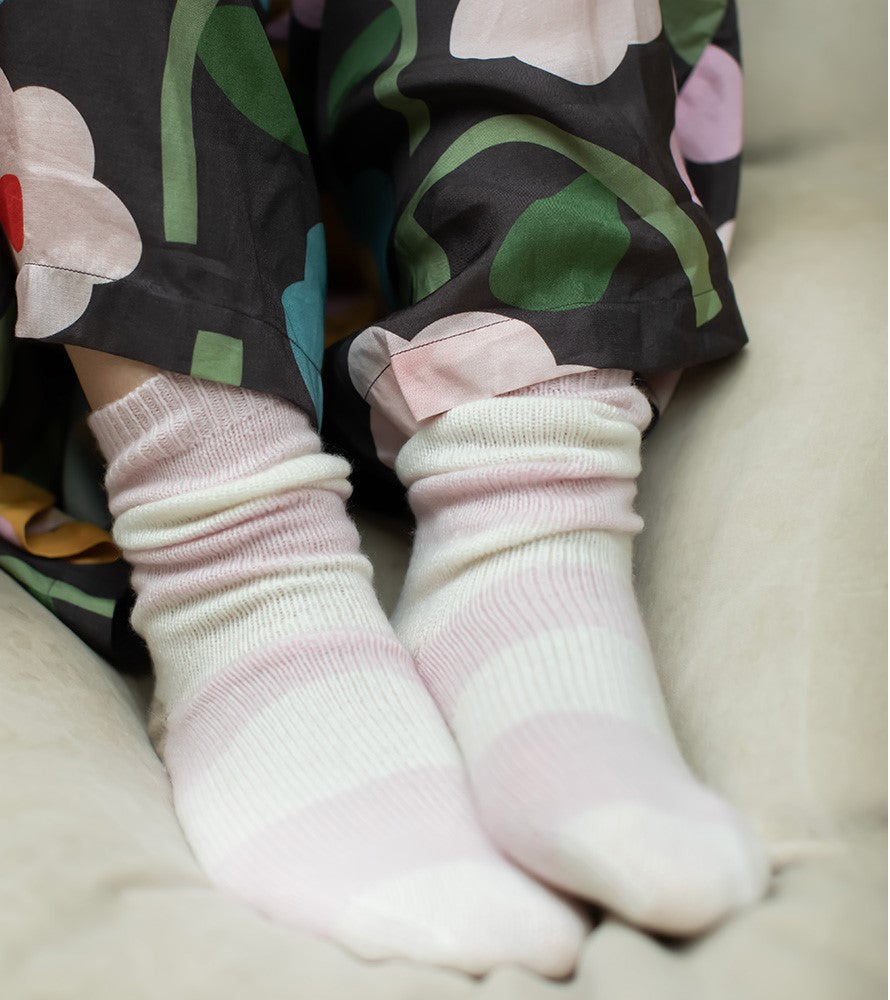 Close-up of feet wearing light pink striped bed socks with floral-patterned pants in the background.