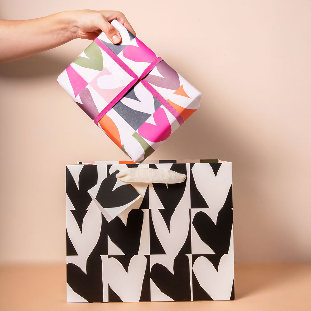 present wrapped in colourful hearts print wrapping paper being placed inside a black & white hearts print gift bag