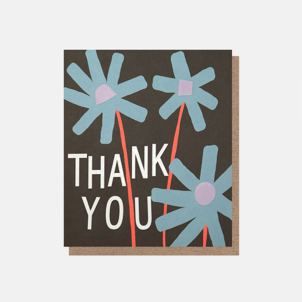 A square thank you card with a dark brown background, featuring three stylized light blue flowers with coral stems and white 'THANK YOU' text, shown with a kraft envelope behind it on a light gray background.