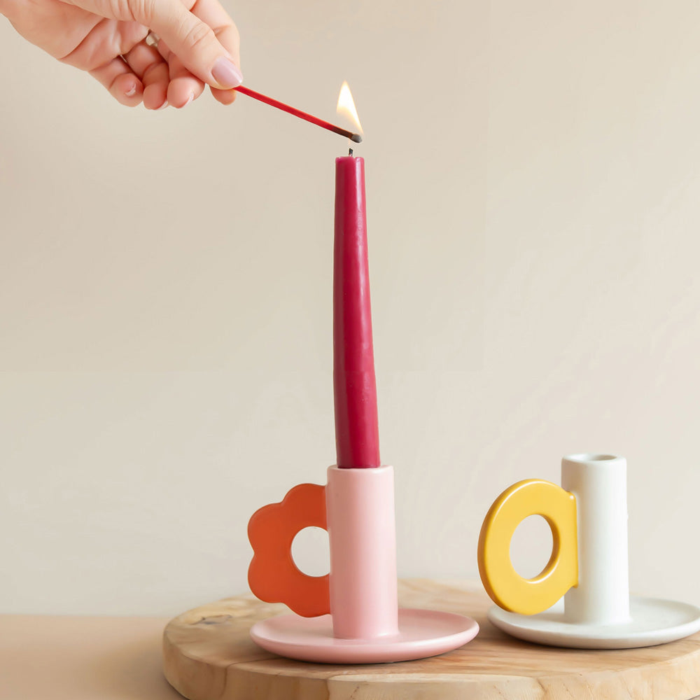 Person lighting a red candle in a pink holder on a wooden surface with a plain background