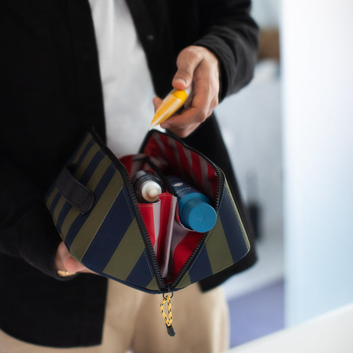 Person holding a striped flat lay ash bag bag with various items inside.