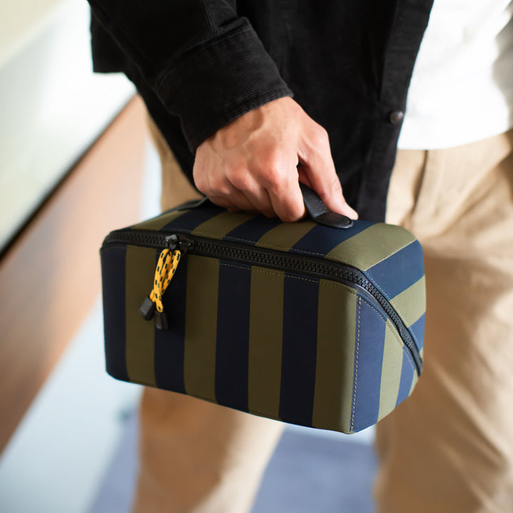 Person holding a striped toiletry bag by grab handle with a blurred background