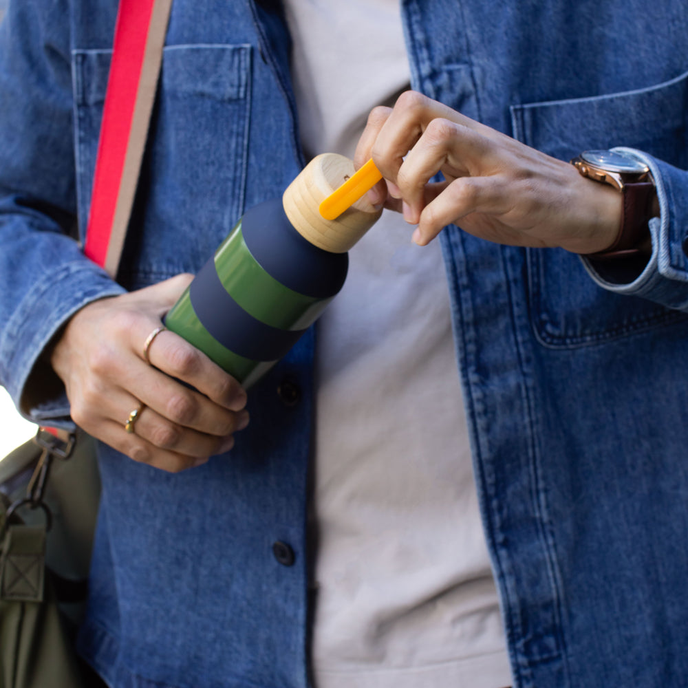 Person holding a colorful striped water bottle with a yellow handle, wearing a blue jacket.