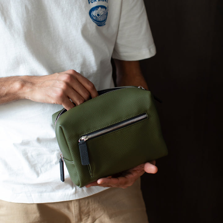 Person holding a green small wash bag with a white shirt in the background
