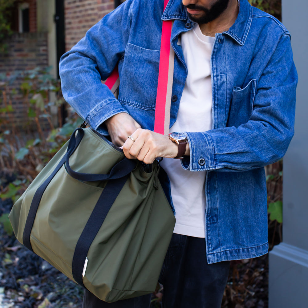 Person holding a green duffel bag with a red strap outdoors.