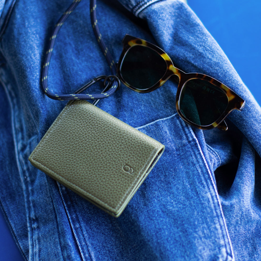Green wallet with lanyard attached and sunglasses on a blue denim surface