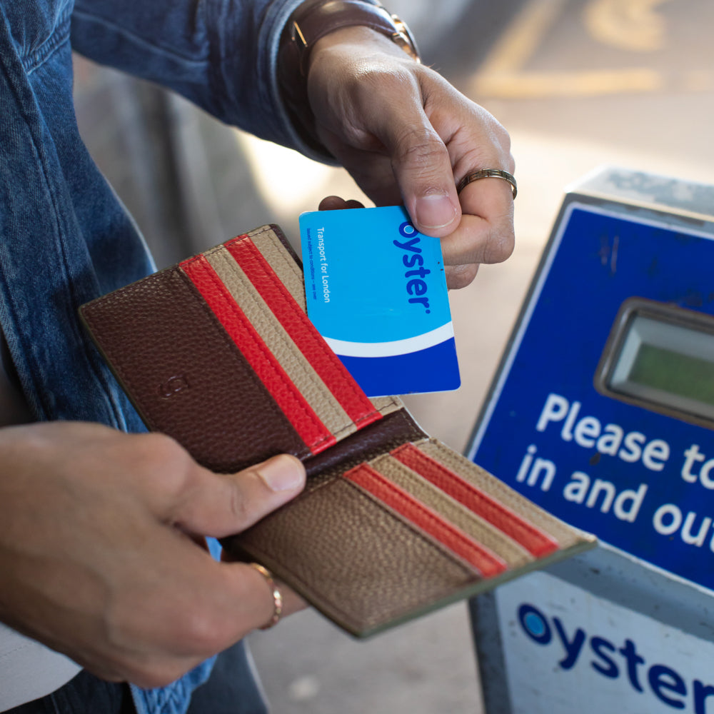 Person using an Oyster card at a fare machine with a brown, red & beige striped wallet.