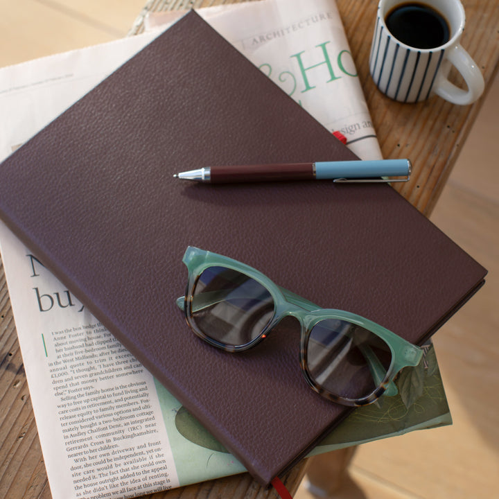 Purple notebook with sunglasses, pen, and coffee cup on a wooden surface