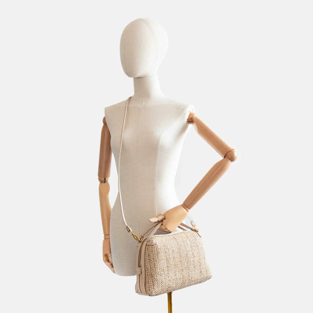 light brown woven straw handbag worn across the body of a mannequin
