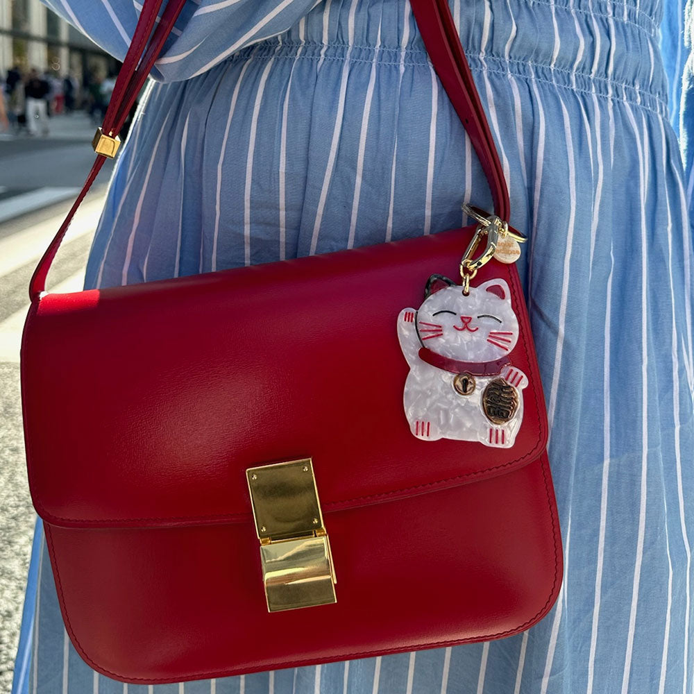 white & red lucky cat bag charm or keyring attached to a red leather handbag