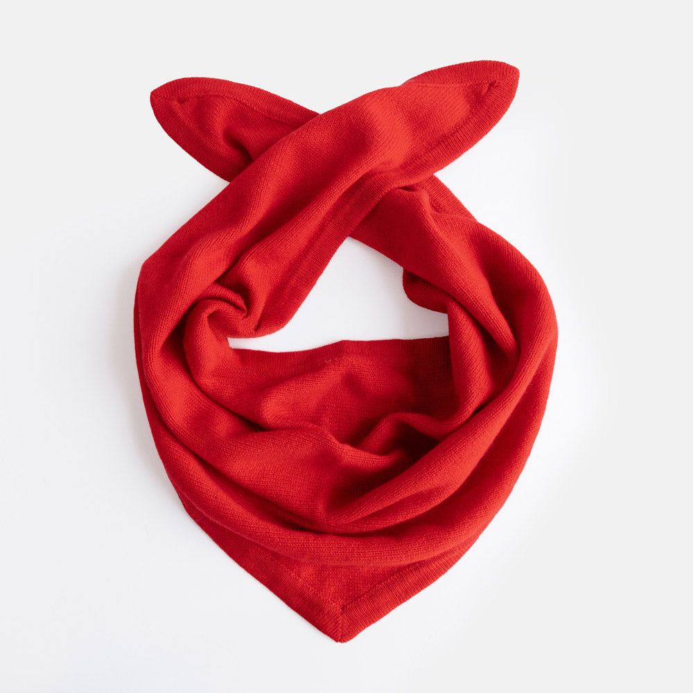 A bright red knit triangle shaped scarf, styled in a loose knot, displayed on a clean white background.