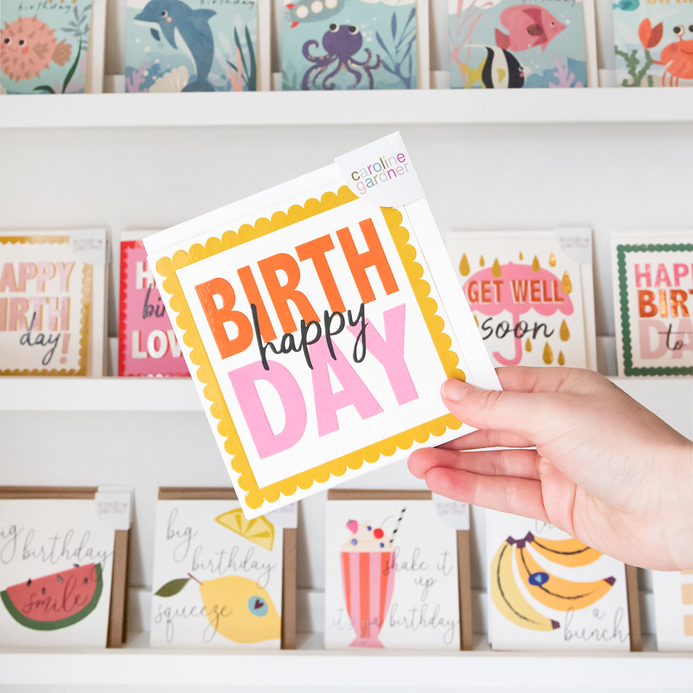 Hand holding a colorful birthday card with more cards displayed in the background.