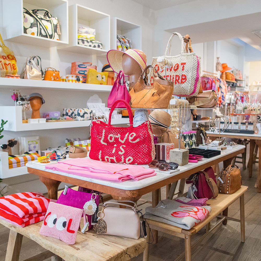 Store interior with various handbags and accessories displayed on tables and shelves.