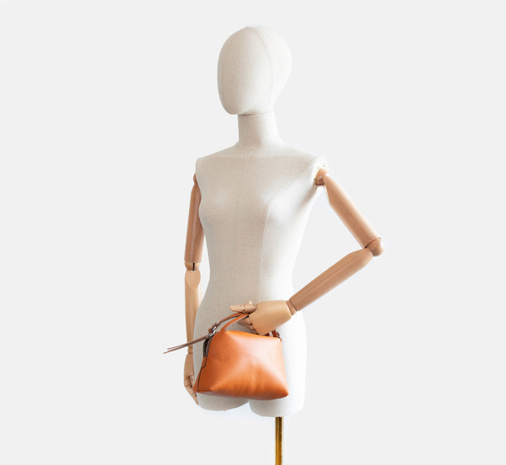 Mannequin holding a orange leather handbag against a white background