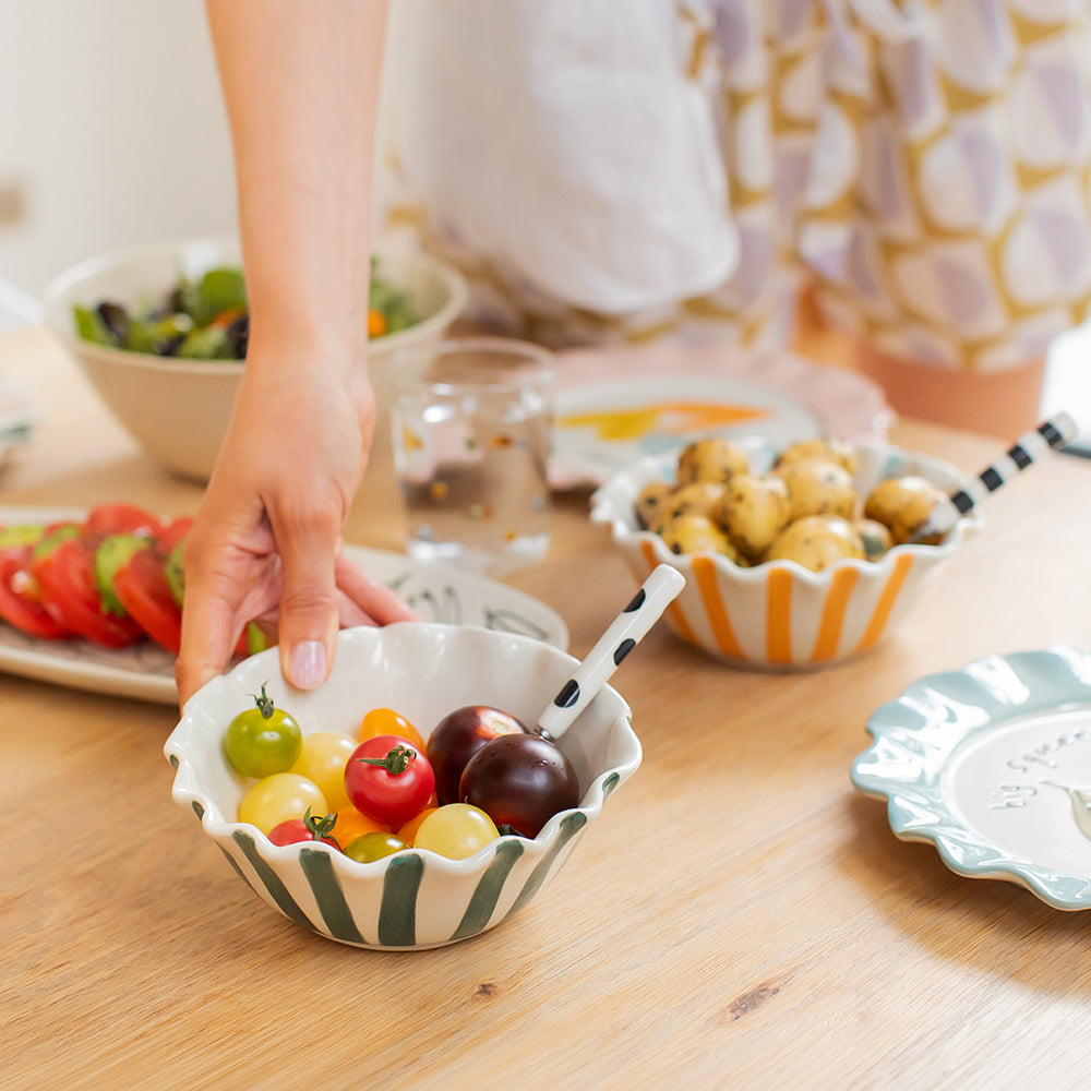 Person holding a small bowl of colorful tomatoes on a wooden table with other food items.